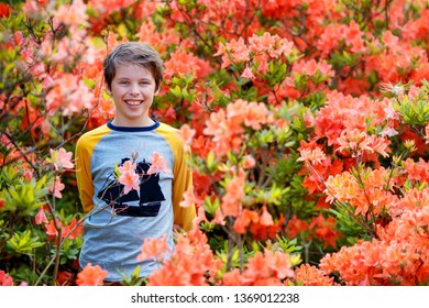 Outdoor Spring Portrait Of Cute Attractive 10 Year Old Boy Posing In The Garden Next To Blossoming Pink Rhododendron