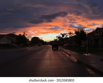 Outdoor Street Photo Of Mid Or After Sunset. Pink And Dark Clouds Mixed With Beautiful Blue Sky. Silhouetted Neighborhood On Street With Reflected Pink Skies On Asphalt And Sidewalk.