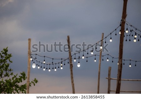 outdoor string lights hanging between rustic wooden posts against a twilight sky. The warm glow of the bulbs contrasts with the cool tones of the dusk sky, creating a cozy and inviting atmosphere.