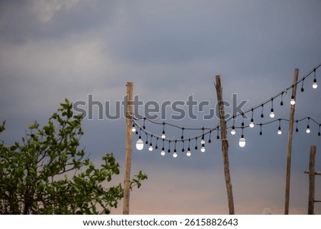 outdoor string lights hanging between rustic wooden posts against a twilight sky. The warm glow of the bulbs contrasts with the cool tones of the dusk sky, creating a cozy and inviting atmosphere.