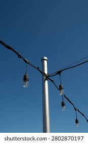 Outdoor string lights that have turned yellow due to rust around them, used for patio lighting, events, or garden decorations—commonly known as festoon lights or Edison bulbs—hanging against a backdrop of a thin, cloudy blue sky