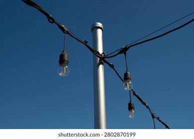 Outdoor string lights that have turned yellow due to rust around them, used for patio lighting, events, or garden decorations—commonly known as festoon lights or Edison bulbs—hanging against a backdrop of a thin, cloudy blue sky