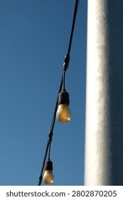 Outdoor string lights that have turned yellow due to rust around them, used for patio lighting, events, or garden decorations—commonly known as festoon lights or Edison bulbs—hanging against a backdrop of a thin, cloudy blue sky
