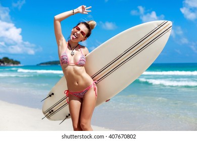 Outdoor summer closeup lifestyle portrait of happy smiling tanned sexy woman posing on the beach with surfboard. Having fun and going crazy. Showing tongue 