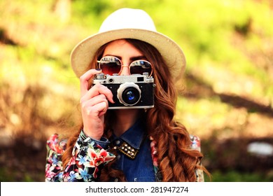 Outdoor Summer Lifestyle Portrait Of Pretty Young Woman Having Fun In The City. Photographer Making Pictures In Hipster Style Glasses And Hat. Photo Toned Style Instagram Filters.
