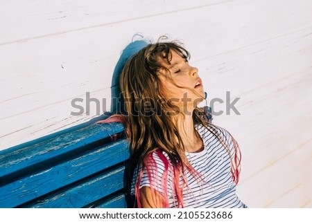 Outdoor summer portrait of cute hait colored girl suffering summer heat. The school girl sits and is exhausted from the heat after outdoor activity while hot sunny day. 