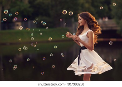 Outdoor summer portrait of young beautiful happy woman making soap bubbles in park or at nature. Joyous happy girl in white dress - Powered by Shutterstock