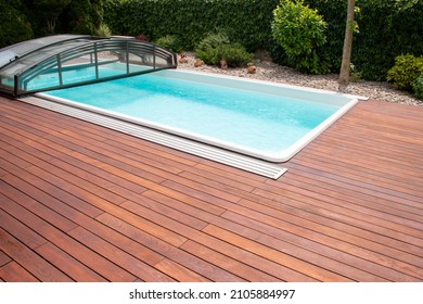 Outdoor swimming pool with cover enclosure and teak wood deck, exotic teakwood flooring stripes around blue water pool - Shutterstock ID 2105884997