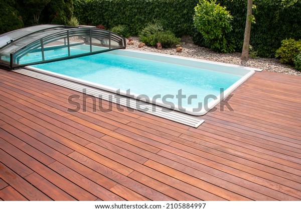 Outdoor\
swimming pool with cover enclosure and teak wood deck, exotic\
teakwood flooring stripes around blue water\
pool