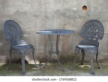 Outdoor Table And Chairs With Dappled Light Against A Concrete Wall