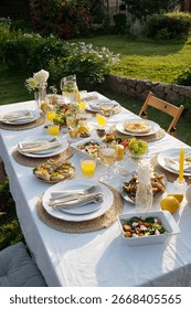 Outdoor table setting displaying assorted salads, fruit, bread, juice, and tableware arranged for group meal, sunlight illuminating fresh food and drinks on tablecloth