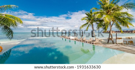 Outdoor tourism landscape. Luxurious beach resort with swimming pool and beach chairs or loungers umbrellas with palm trees and blue sky, sea horizon. Summer island relax travel and idyllic vacation 