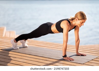 Outdoor Training. Sporty Middle Aged Female Standing In Plank Position On Fitness Mat While Exercising On Wooden Pier Near River, Beautiful Woman In Activewear Strength Her Abs Muscles, Copy Space - Powered by Shutterstock