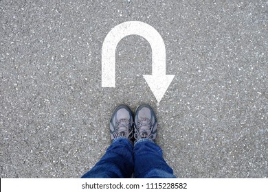 Outdoor trekking shoes standing on the asphalt concrete floor in front of u turn symbol.