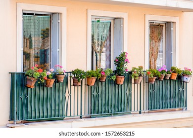 Outdoor view of three typical french windows decorated with painted thread beaded blinds and wrought-iron aquamarine balconies with geranium flowerpots on peach colored wall