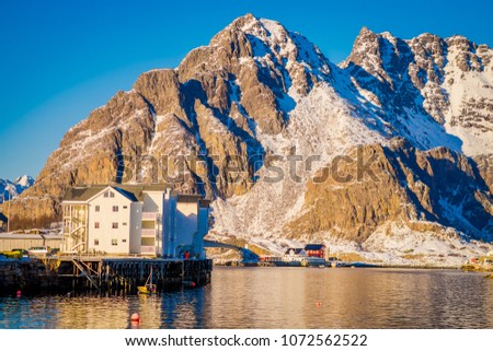 Outdoor view of a white building in the shore with a huge mountaing behind in Henningsvaer on Lofoten islands