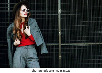 Outdoor Waist Up Portrait Of Beautiful Woman Posing On Street. Model Wearing Stylish Red, Grey Classic Clothes, Wide-brimmed Hat, Round Sunglasses. Female Fashion Concept. Copy, Empty Space For Text