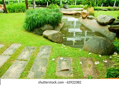 Outdoor Walkway Among It's Raining In The Green Garden With A Small Pond.