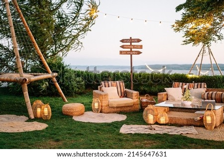Outdoor wedding. Banquet. signs on wooden board decorated by flowers and greenery and lounge zone in boho style including chairs and tables.