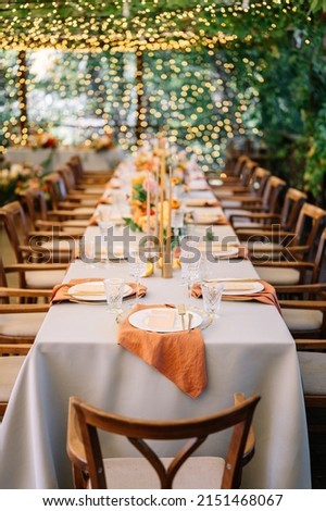 outdoor wedding. long banquet tables with white tablecloths , on the tables are flower arrangements, candles, plates with napkins, glasses and cutlery in autumn style