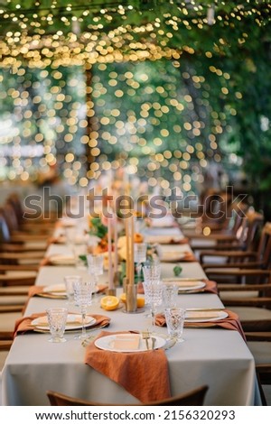 outdoor wedding. long banquet tables with white tablecloths , on the tables are flower arrangements, candles, plates with napkins, glasses and cutlery in autumn style
