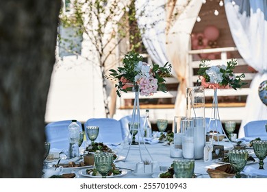 Outdoor wedding reception table setting floral centerpiece elegant decor white tablecloths green glassware candles plates with salads blurred background trees draped curtains festive atmosphere - Powered by Shutterstock