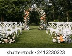 Outdoor wedding setup with floral arch. Wedding aisle with white wooden chairs.