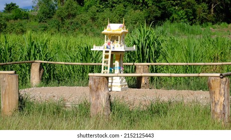Outdoor white holy spiritual Thai spirit house inside log fence in the field with green grass in the back for evil protection. Concept in good faith, family and household protection, and good health. 