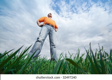 Outdoor Wide-angle Portrait Of A Tall Man In Jeans On Blue Sky And Green Grass Background