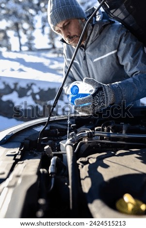 Outdoor winter scene of man pouring antifreeze windshield liquid. Car maintenance concept.