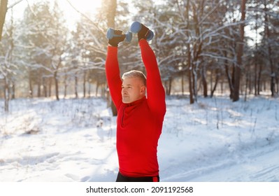 Outdoor Winter Sports. Athletic Senior Man Working Out With Dumbbells, Training Arm Muscles At Snowy Forest. Strong Mature Guy Lifting Weights, Pumping Strength In Cold Weather Outside