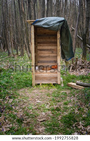 Outdoor wooden toilet surrounded by trees in a forest. Portrait photo.