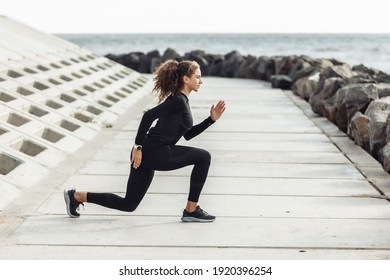 Outdoor workout concept. Fit slim woman with curly hair stretches or warms up on an urban embankment with concrete slabs