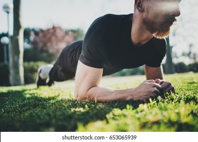 Outdoor Workout Lifestyle Concept.Young Bearded Man Doing Abdominal Exercises Before Training.Muscular Athlete Exercising Outside In Sunny Park. Blurred Background.Horizontal