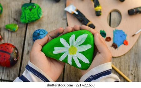 Outdoor workshop in summer. A selective focus of a schoolboy boy holding a painted flat stone in his hands. Do it yourself. - Powered by Shutterstock