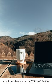 Outdoor Workspace With Laptop, Coffee And Smartphone On A Wooden Table In The Mountain