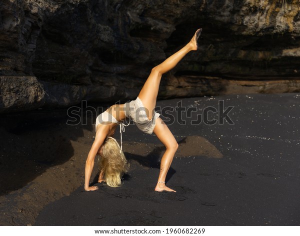 Outdoor yoga. Caucasian woman practicing Eka\
Pada Chakrasana, One Legged Wheel Pose. Upward facing bow pose is a\
deep backbend. Flexible, strong body. Yoga retreat. Copy space.\
Bali beach, Indonesia