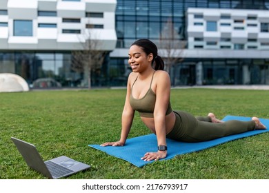 Outdoor Yoga Practice. Flexible Young Black Woman Doing Cobra Pose, Following Online Sports Video On Laptop At City Park, Copy Space. Millennial Lady Exercising, Keeping In Perfect Shape Outside