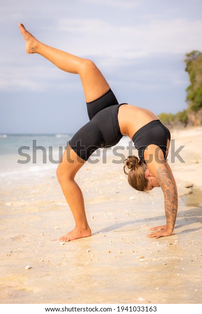 Outdoor\
yoga. Young woman practicing Eka Pada Chakrasana, One Legged Wheel\
Pose. Upward facing bow pose is a deep backbend. Flexible, strong\
body. Yoga retreat. Thomas beach, Bali,\
Indonesia