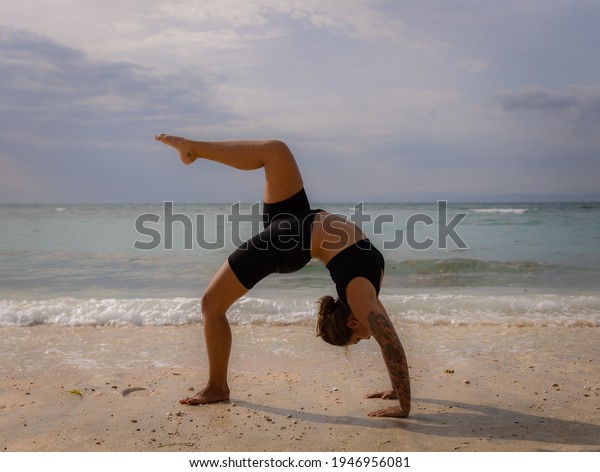 Outdoor\
yoga. Young woman practicing Eka Pada Chakrasana, One Legged Wheel\
Pose. Upward facing bow pose is a deep backbend. Flexible, strong\
body. Yoga retreat. Thomas beach, Bali,\
Indonesia