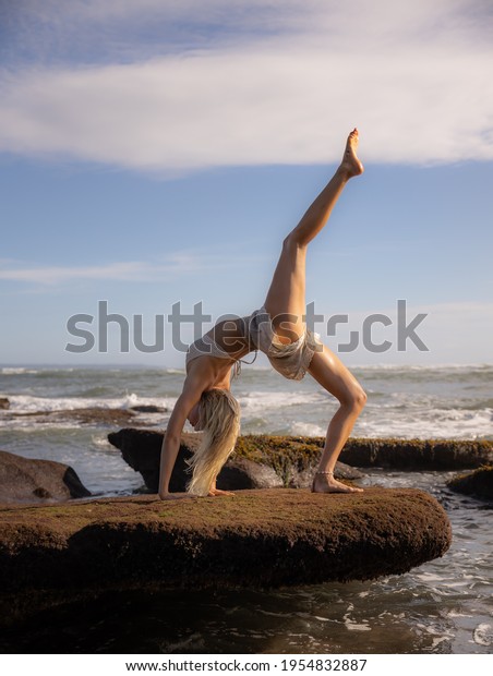 Outdoor yoga. Young woman practicing Eka Pada\
Chakrasana, One Legged Wheel Pose. Upward facing bow pose is a deep\
backbend. Flexible, strong body. Yoga retreat. Copy space. Beach in\
Bali, Indonesia