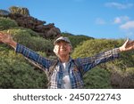 Outdoors activity in nature. Carefree caucasian senior woman with backpack enjoying trekking day in a green countryside admiring landscape with open arms, Healthy lifestyle in retirement concept