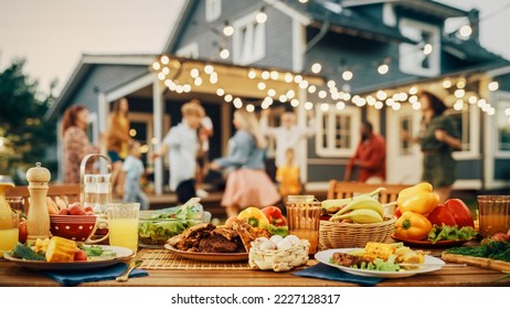 Outdoors Dinner Table with Gorgeous-Looking Barbecue Meat, Fresh Vegetables and Salads. Happy Joyful People Dancing to Music, Celebrating and Having Fun in the Background on Home Porch.