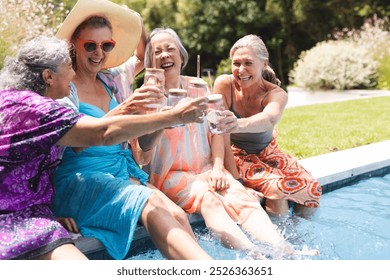 Outdoors, diverse senior female friends laughing, toasting by pool. Wearing colorful summer clothes against blue background, theyre enjoying a sunny day together, creating memories in vibrant attire, - Powered by Shutterstock