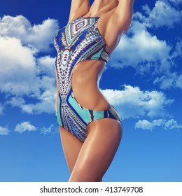 Outdoors fashion photo of young lady with perfect body in swimsuit against the sky