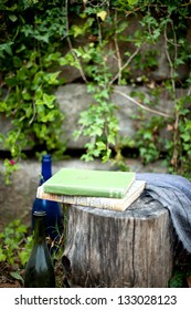 outdoors picnic nook with green vines, wood stump seat, books and wine bottles