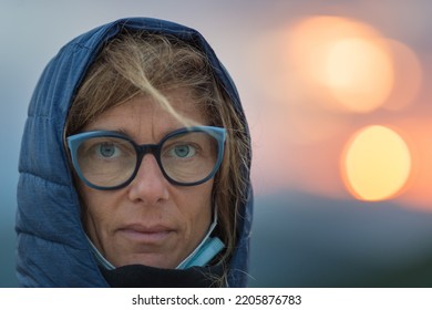 Outdoors Portrait Of Adult Mid Age Woman With Blue Green Eyes, Wearing Glasses. Defocused Backgropund, Serious Facial Expression.