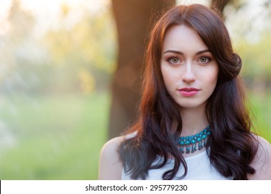 Outdoors portrait of beautiful young brunette woman looking at camera.