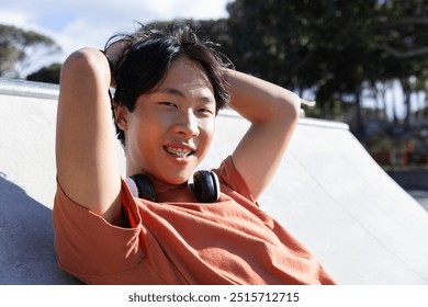 Outdoors, Relaxing at skatepark, asian teenage boy with braces and headphones smiling. skateboarding, skateboarder, teenager, outdoor, leisure, urban - Powered by Shutterstock