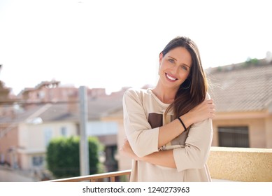 Outdoors shot of friendly looking timid woman, smiles from happiness and joy, hugs herself, feels shy, has long hair, lives perfect life. Positive emotions